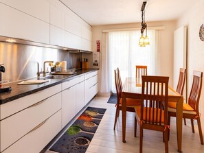 A modern kitchen with a dining area, including a table and chairs, and a window with curtains.