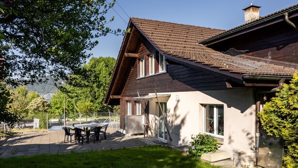 A two-story house with a tiled roof, a patio with outdoor furniture, and a view of a lake. - Hauswurz by Interhome (Gwatt (Thun))