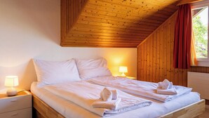 A bedroom with a wooden ceiling, a bed with white linens, two bedside tables with lamps, and a window with curtains. - Hauswurz by Interhome (Gwatt (Thun))