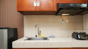 A kitchen with wooden cabinets, a stainless steel sink, a toaster, and a refrigerator. - Beautiful Studio at Cosmo Terrace Apartment (Jakarta)