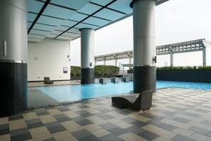 An indoor swimming pool with checkered flooring, lounge chairs, and a covered area with pillars. - Cozy Living Studio at Cosmo Terrace Apartment (Jakarta)
