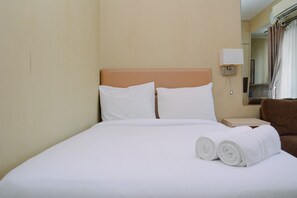 A hotel room with a bed, two pillows, a nightstand, a lamp, and a brown chair. - Cozy Living Studio at Cosmo Terrace Apartment (Jakarta)