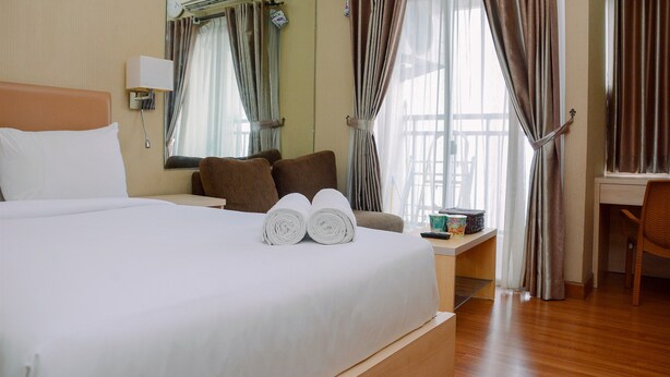 Ein Hotelzimmer mit einem großen Bett, einem Schreibtisch, einem Stuhl und einem Fenster mit Vorhängen.
