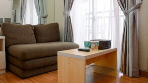 Ein modernes Wohnzimmer mit einer Couch, einem kleinen Holztisch und einem Fenster mit Vorhängen.