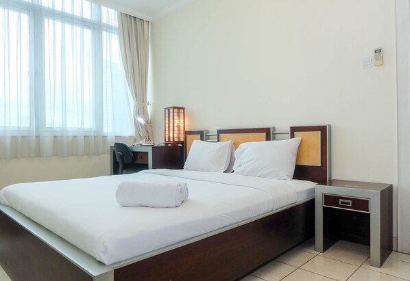Una habitación de hotel con una cama grande, una mesita de noche con lámpara y una ventana con cortinas.