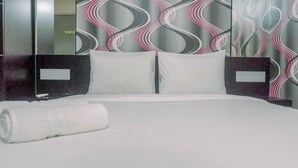 Un lit bien fait, avec du linge de lit blanc et des oreillers, une serviette blanche roulée, et un mur moderne orné d’un motif ondulé.