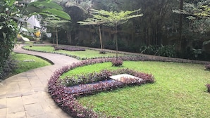 A landscaped garden with a curved pathway, manicured grass, and various shrubs. - Spacious & Comfy 2BR at Galeri Ciumbuleuit Apartment (Bandung)