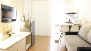 A compact living space with a kitchenette, a flat-screen TV mounted on the wall, a sofa, and a dining area with chairs.
