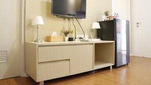 A modern room with a flat-screen TV mounted on the wall, a wooden cabinet with a built-in phone, and a refrigerator.
