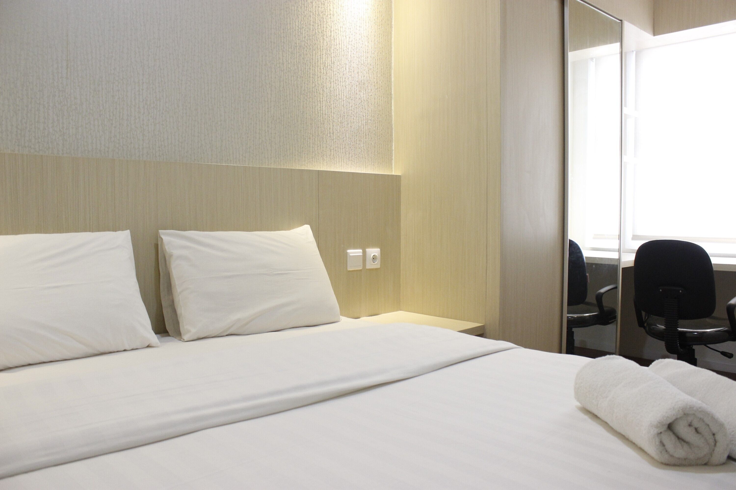 A hotel room with a neatly made bed, a bedside table, a chair, and a large mirror.