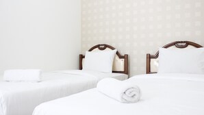 Habitación de hotel con dos camas individuales, cada una con cabecero de madera, ropa de cama blanca y una toalla enrollada en blanco.