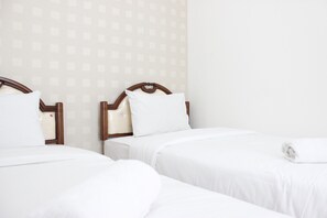 Habitación de hotel con dos camas individuales, cada una con cabecero de madera y ropa de cama blanca.