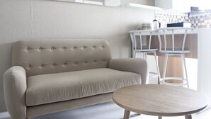 Un salón moderno con un sofá beige, una mesa redonda de madera y taburetes blancos.