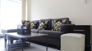 Ein modernes Wohnzimmer mit einem grauen Sofa, einem kleinen weißen Hocker, einem Couchtisch und einer schwarzen Kommode.