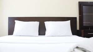 Ein ordentlich bezogenes Bett mit weißer Bettwäsche und zwei Kissen, ein dunkles Kopfteil und ein dunkler Nachttisch zur Rechten.