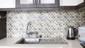 A kitchen with a tiled backsplash, stainless steel sink, and a kettle. - Modern Studio Room at Tamansari La Grande Apartment (Bandung)