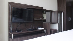 A modern entertainment unit with a flat-screen TV, multiple electronic devices, and built-in shelving. - Modern Studio Room at Tamansari La Grande Apartment (Bandung)