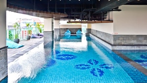 Une piscine intérieure à l’eau d’un bleu cristallin, entourée de murs recouverts de carreaux et d’une terrasse en bois.