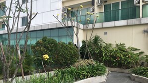 Une cour intérieure agrémentée de diverses plantes et arbres, un chemin bordé de dalles et un bâtiment doté de grandes fenêtres et de climatiseurs.