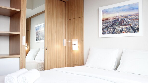 Une chambre d’hôtel avec un lit, une armoire en bois et un tableau représentant un paysage urbain accroché au mur.