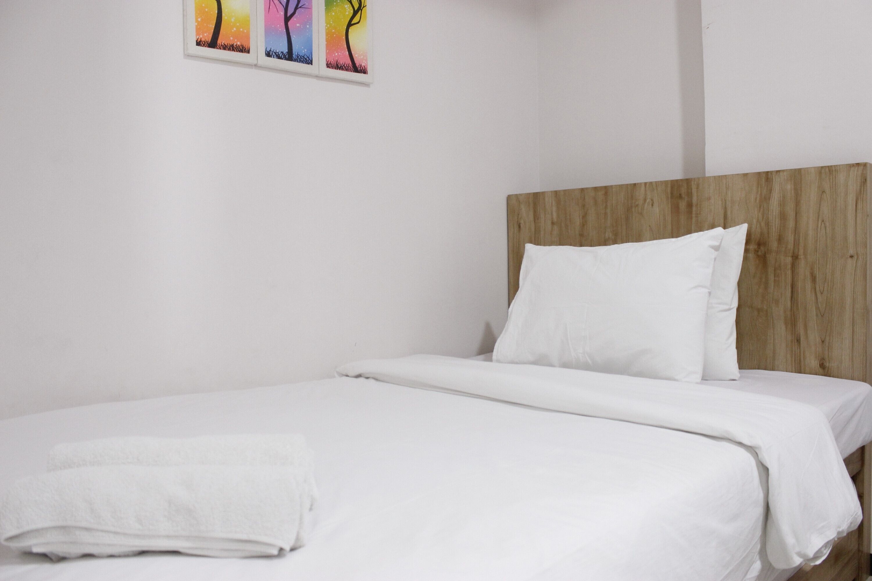 A neatly made bed with white linens and pillows, a wooden headboard, and a wall-mounted painting of trees.