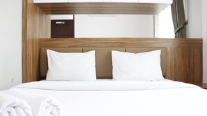 Una cama bien hecha con sábanas y almohadas blancas, un cabecero de madera y toallas blancas enrolladas sobre la cama.