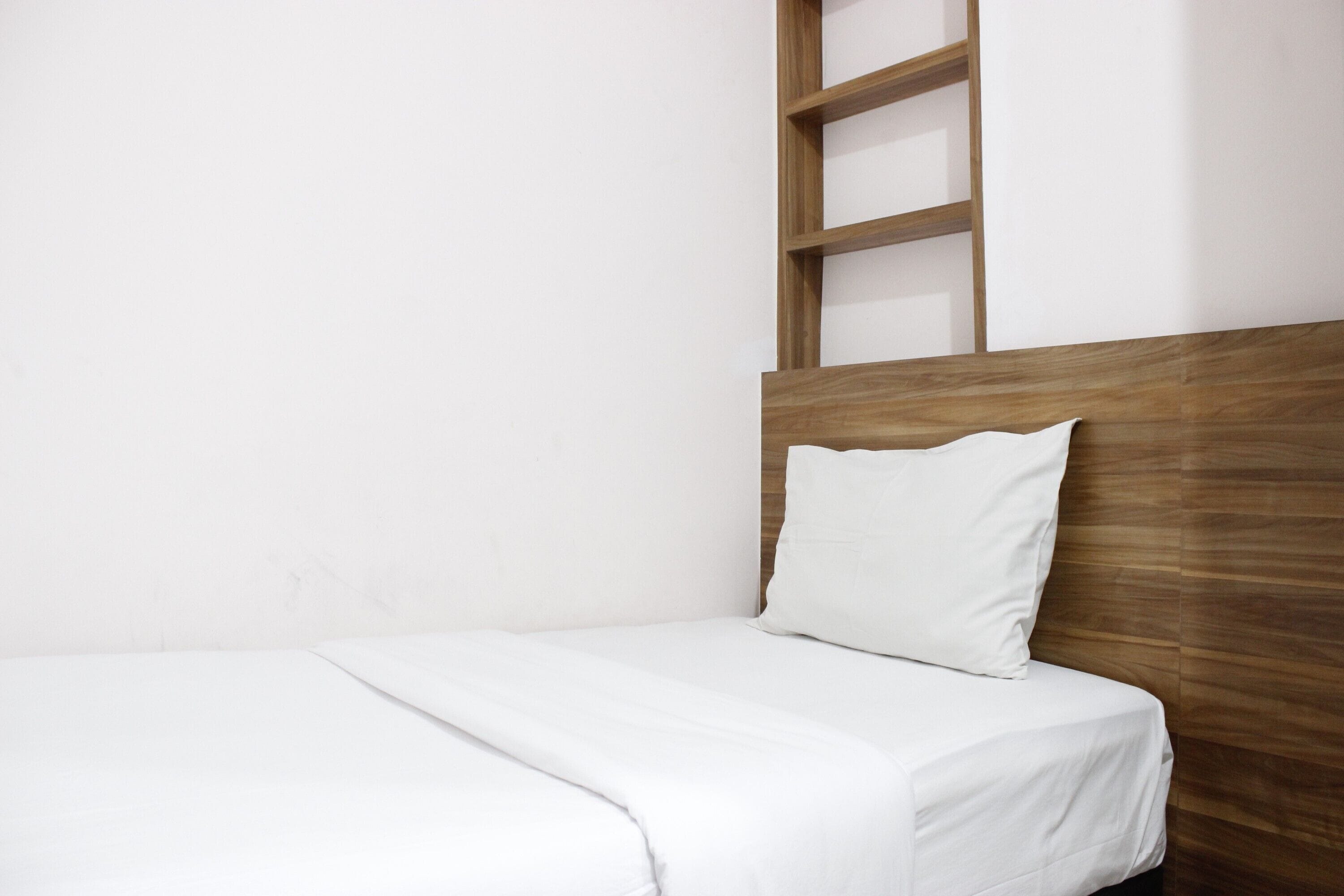 A single bed with a wooden headboard and white bedding in a room with plain white walls.