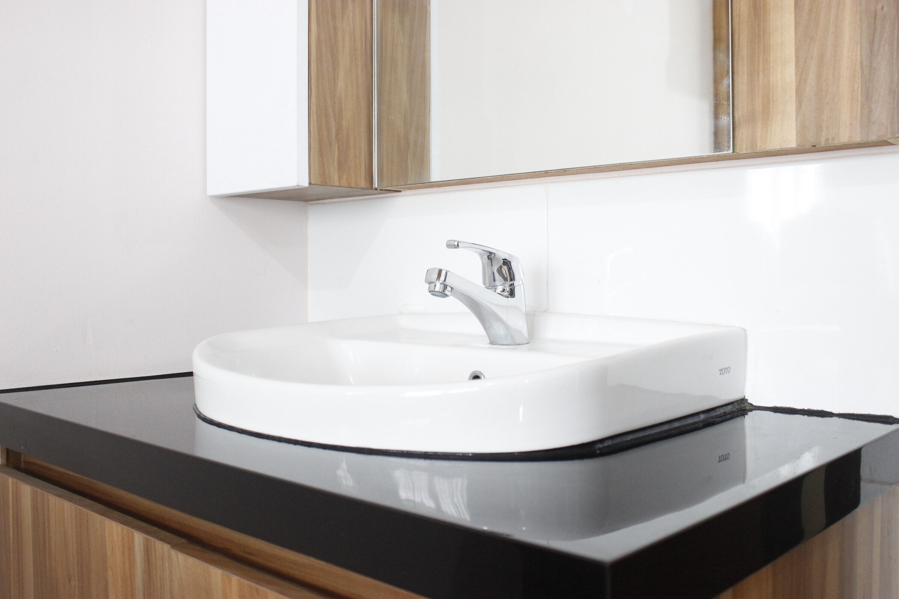 A modern bathroom with a white sink, black countertop, and wooden cabinets.