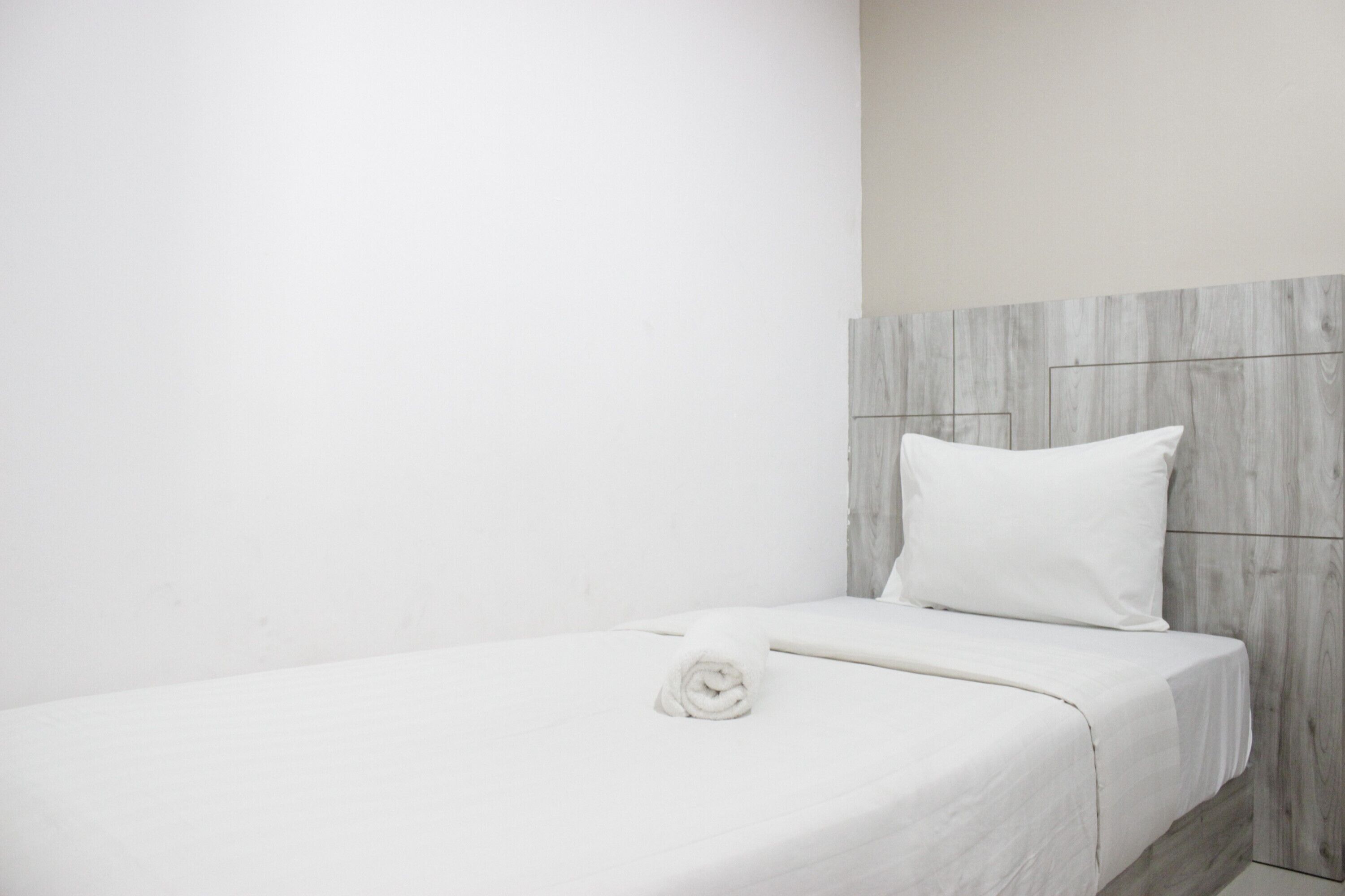 A single bed with a white mattress and a neatly folded white towel.