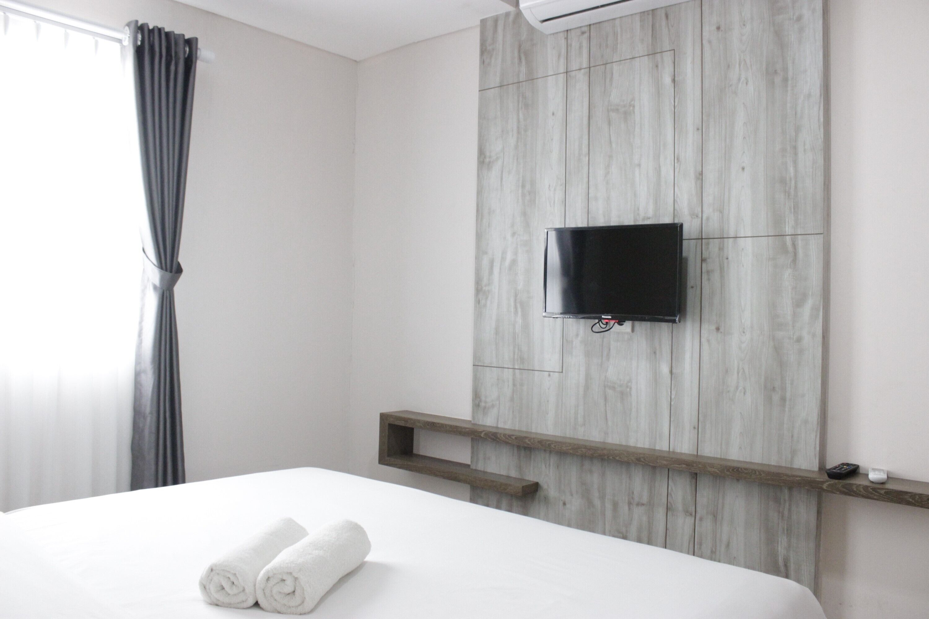Une chambre d’hôtel avec un lit, un téléviseur fixé au mur, un mur recouvert de panneaux en bois et une fenêtre avec des rideaux.