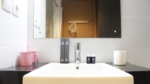 A bathroom with a white sink, a mirror, a pink mug, and two toiletry bottles. - Scenic & Comfy Studio At Beverly Dago near ITB (Bandung)