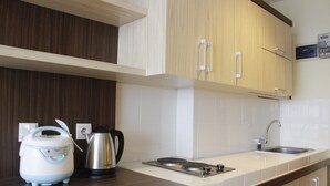 A modern kitchen with wooden cabinets, a stainless steel kettle, a coffee maker, and a sink. - Scenic & Comfy Studio At Beverly Dago near ITB (Bandung)