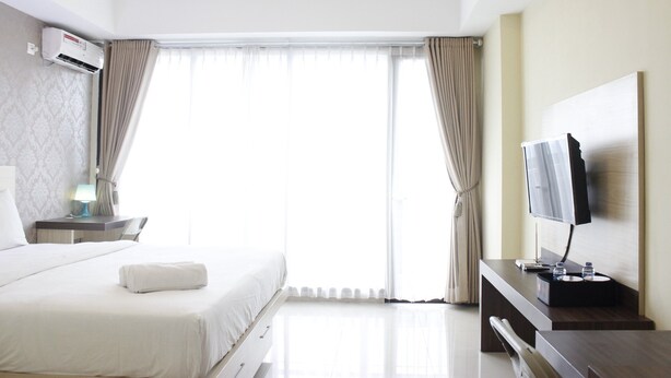 A hotel room with a bed, a desk, a TV, and a window with curtains. - Scenic & Comfy Studio At Beverly Dago near ITB (Bandung)