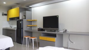 Una cocina moderna con refrigerador, estufa y un televisor de pantalla plana. Hay dos taburetes y una cama en la habitación.