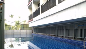 Una piscina con borde de azulejos, rodeada por una valla de metal, y contigua a un edificio con balcones.