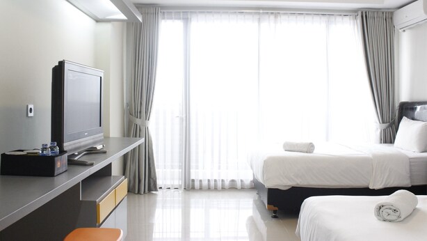 Habitación de hotel con cama, escritorio con televisor y ventana con cortinas.