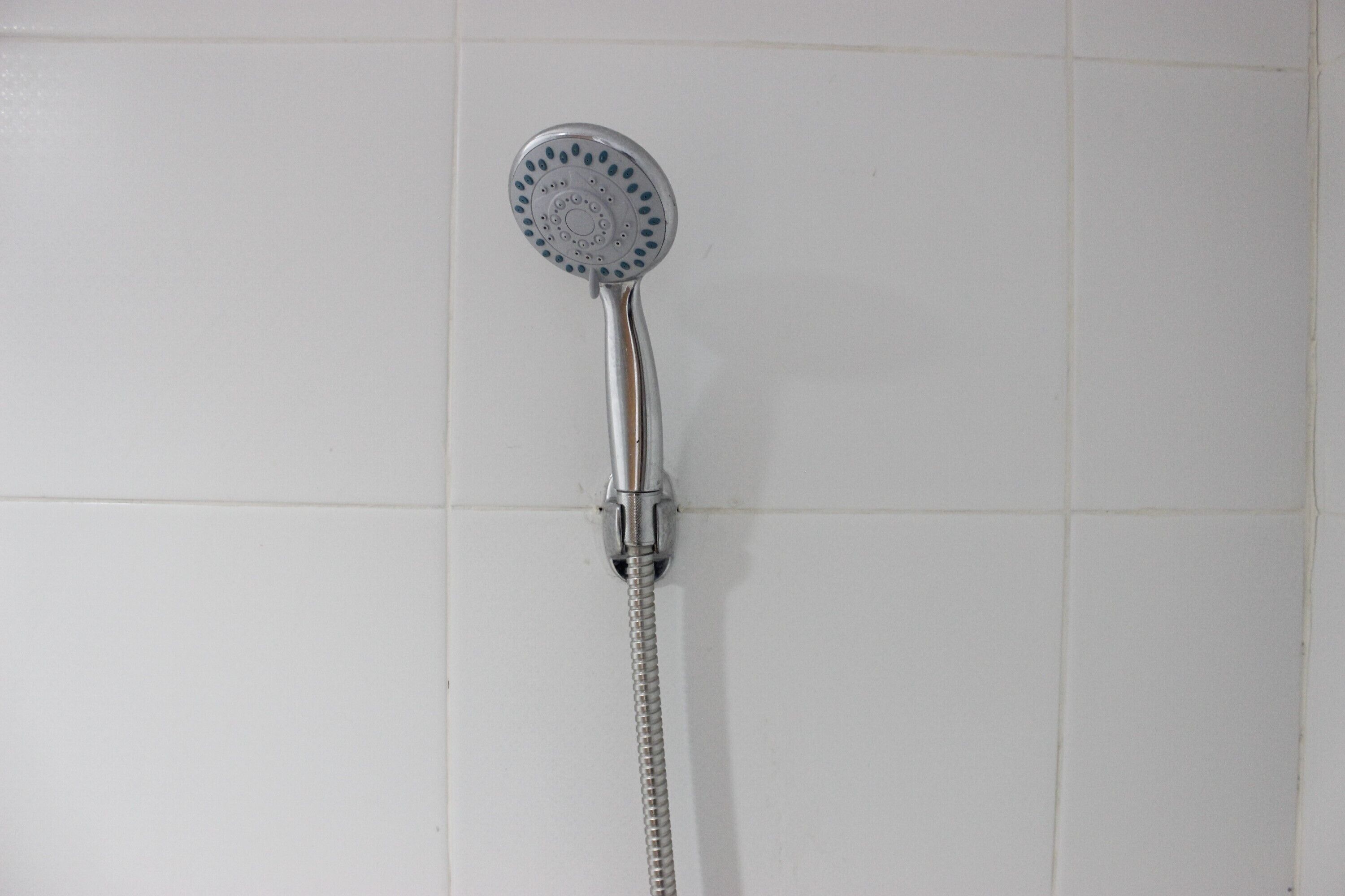 Ein Duschkopf mit flexiblem Schlauch, an einer gefliesten Wand befestigt.