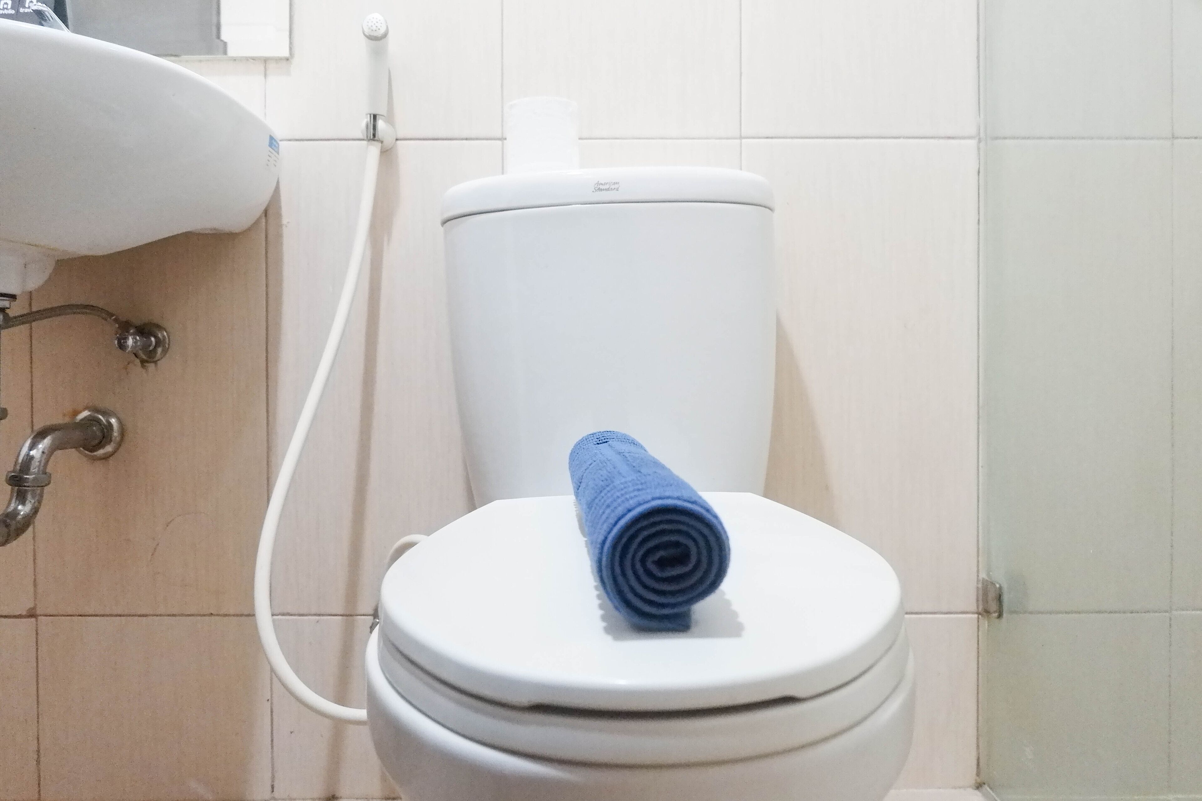 A white toilet with a blue towel on the lid, a white sink, and a visible pipe.