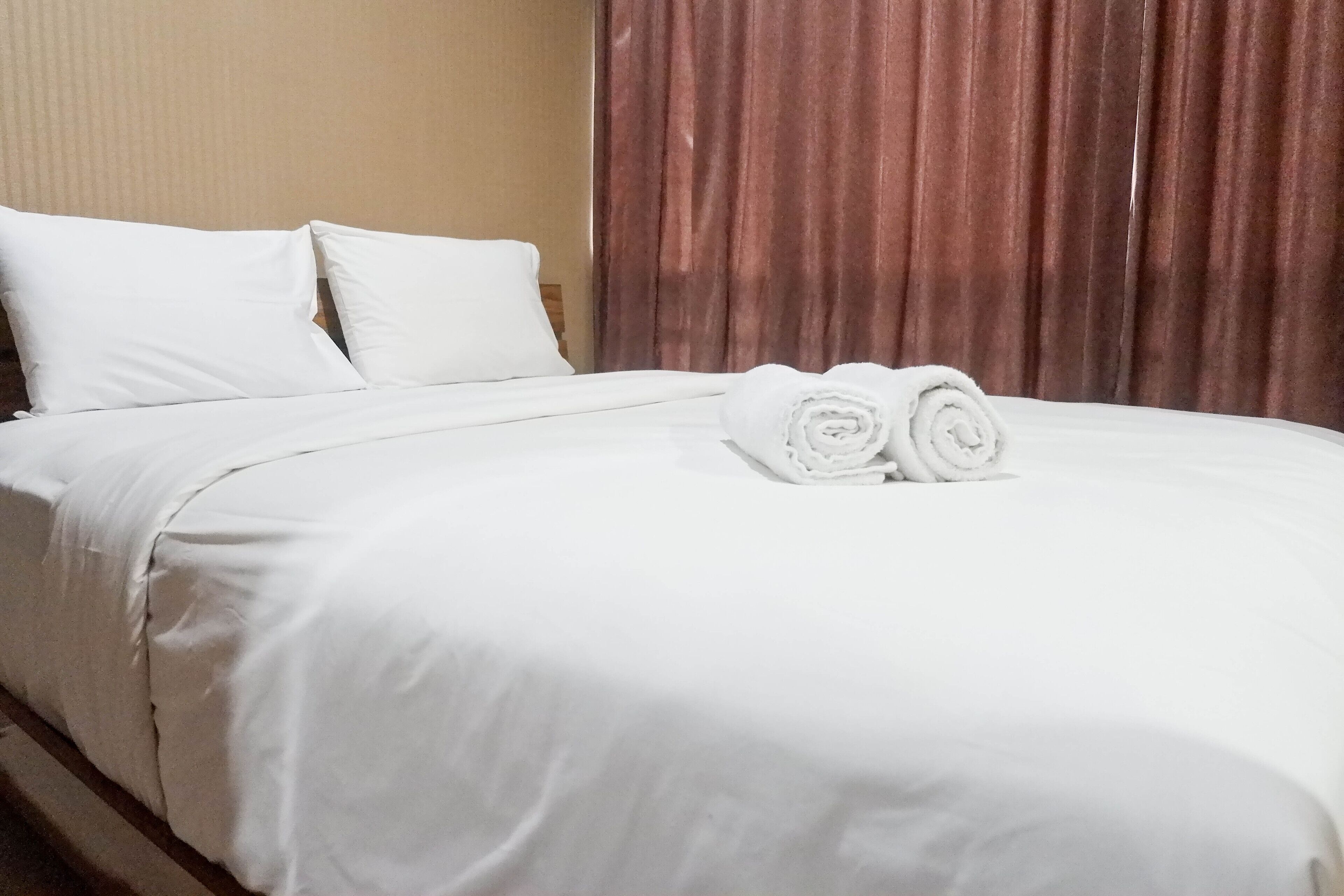 A neatly made bed with white linens and two rolled towels placed at the foot of the bed.