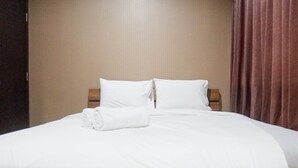 Una cama bien hecha con ropa blanca y almohadas, cabecera de madera y pared marrón.