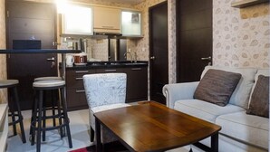 Un espacio habitable compacto con kitchenette, una zona de comedor con taburetes, un sofá y una mesa de centro.