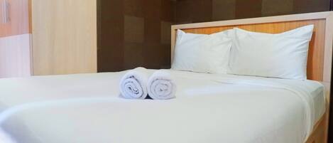 A neatly made bed with white linens and two rolled towels placed at the foot of the bed.