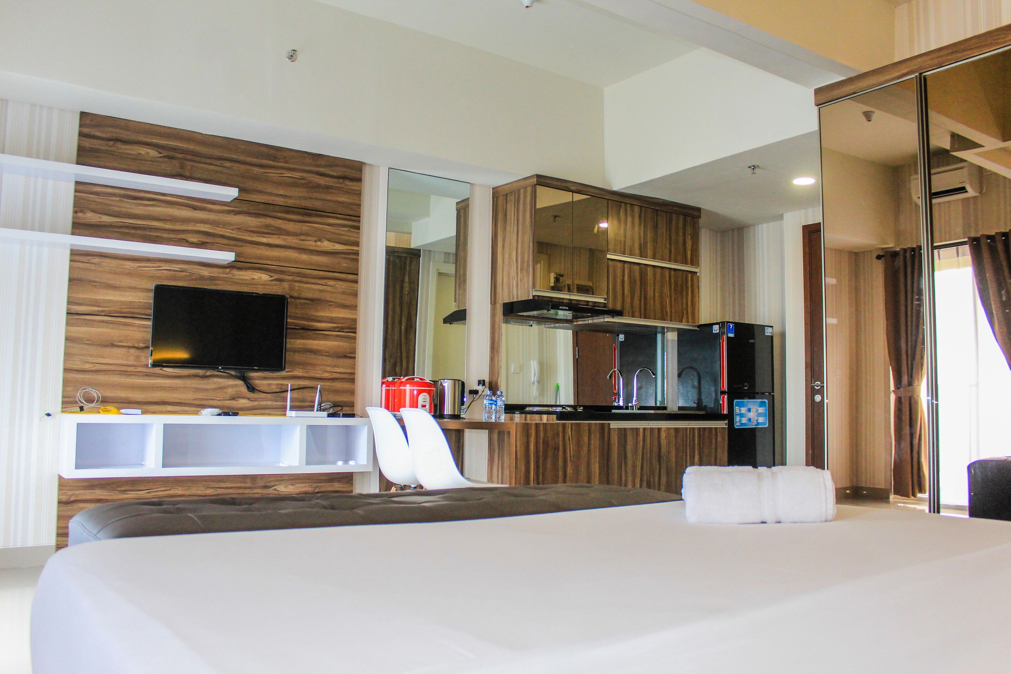 A modern hotel room with a large bed, a flat-screen TV mounted on the wall, a built-in kitchen with a microwave, and a separate bathroom area.