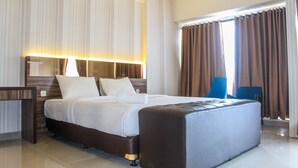 A modern hotel room with a large bed, a nightstand, a desk, and a view of the outdoors through curtains. - Minimalist and Stylish Studio Parkland Avenue Apartment (South Tangerang)