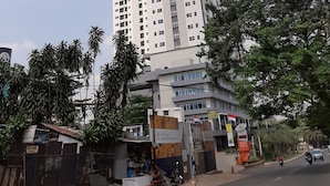 A tall, modern building with multiple floors, surrounded by greenery and a street with vehicles. - Minimalist and Stylish Studio Parkland Avenue Apartment (South Tangerang)