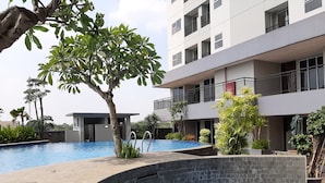 A modern building with a swimming pool, surrounded by greenery and a clear sky. - Minimalist and Stylish Studio Parkland Avenue Apartment (South Tangerang)