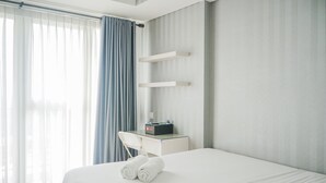 Une chambre d’hôtel avec un lit, un bureau et une chaise, une radio et une fenêtre avec des rideaux.
