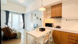 A modern kitchen with wooden cabinets, a white countertop, and a dining area with a table and chairs. - Minimalist and Comfortable 1BR Casa De Parco Apartment (Pagedangan)