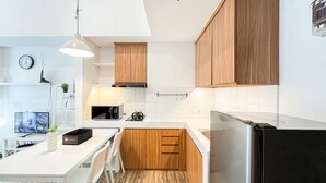 A modern kitchen with wooden cabinets, a white countertop, a microwave, and a refrigerator. - Minimalist and Comfortable 1BR Casa De Parco Apartment (Pagedangan)