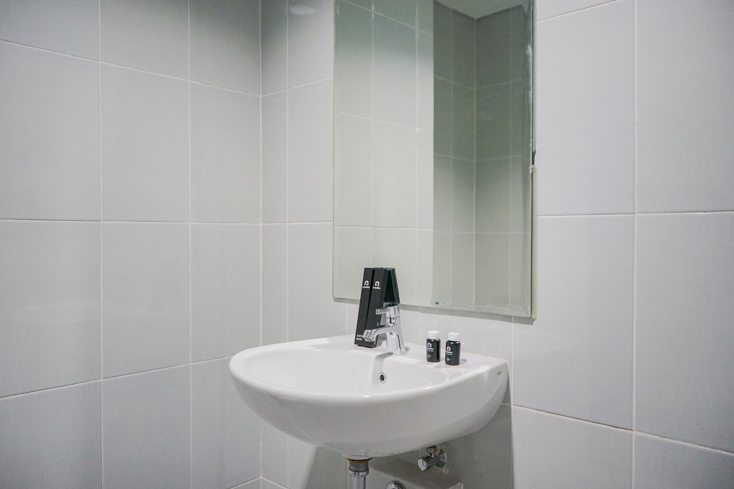 Un baño con un lavamanos blanco, un espejo y dos artículos de tocador sobre el lavamanos.